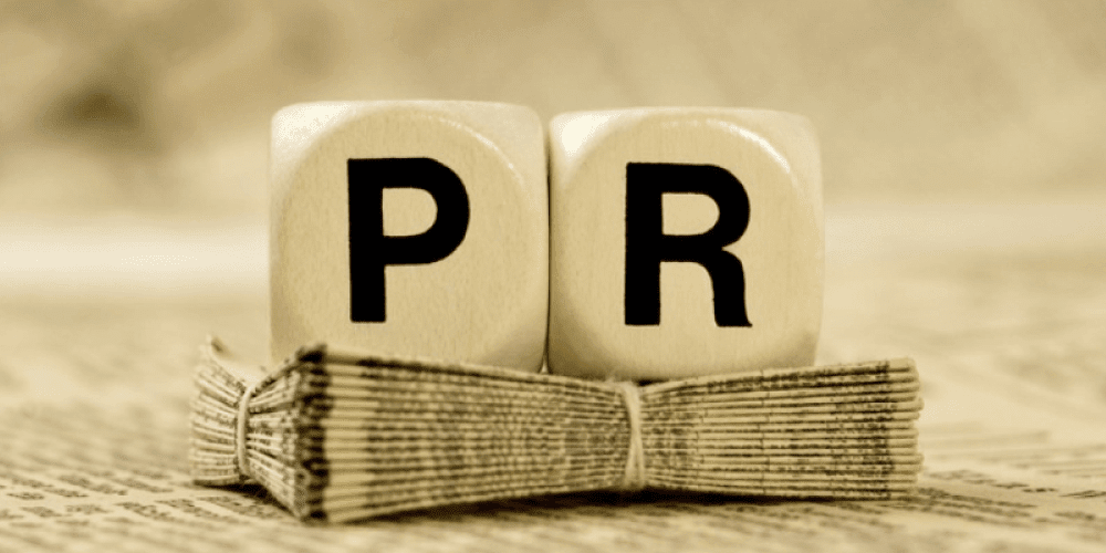Wooden letter blocks spelling PR stacked on a bundle of newspapers, representing a public relations strategy for Tulsa businesses